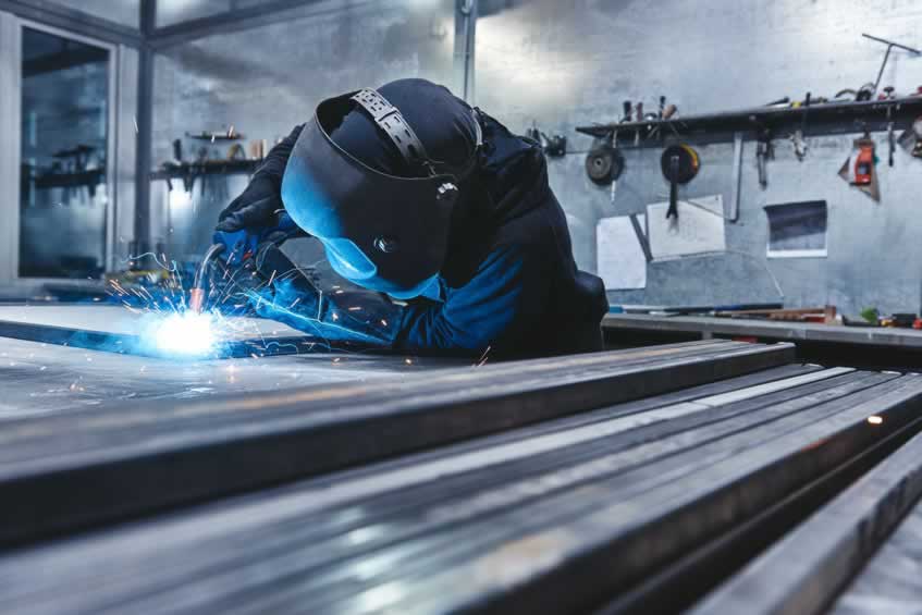 Male worker wearing helmet and gloves welding steel construction at the factory